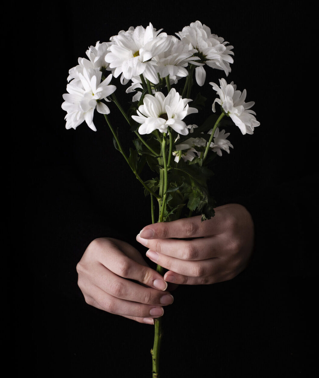 Ramo de flores blancas sostenido con las manos sobre fondo oscuro.